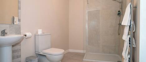 A bathroom with a toilet, sink, shower, and a towel rack.