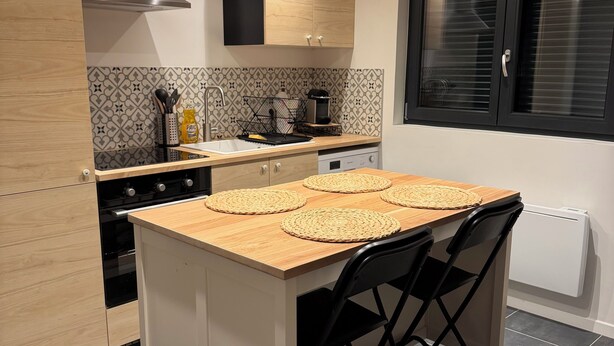 Moderni keittiö, jossa on keskellä sijaitseva saareke, mustat tuolit ja ikkuna, jossa on sälekaihtimet.