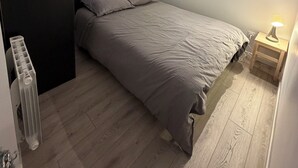 Makuuhuone, jossa on sänky, yöpöytä lampun kanssa, patteri ja kattovalokuvio.
