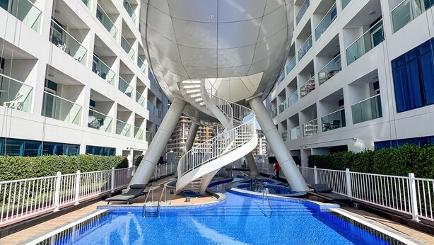A modern building with a circular atrium, a central pool, and a spiral staircase. - PVH - Opalz by Danube 1BR with Jacuzzi (Dubai)
