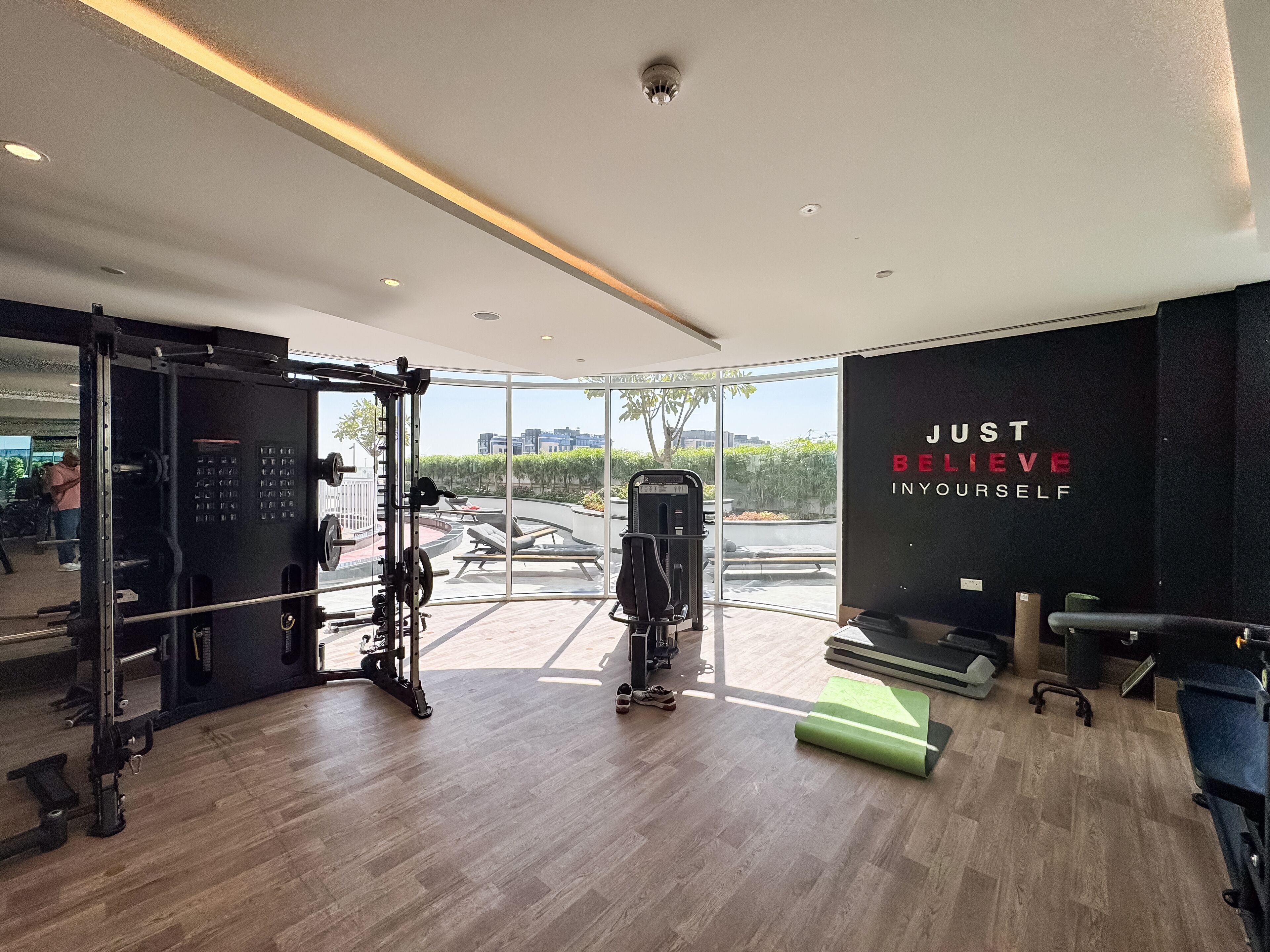 Ein modernes Fitnessstudio mit unterschiedlichen Trainingsgeräten, einer motivierenden Wand und Blick ins Freie.