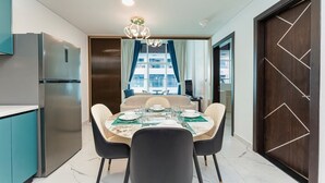 A modern dining area with a round table set for four, a built-in refrigerator, and a large window with curtains. - PVH - Opalz by Danube 1BR with Jacuzzi (Dubai)