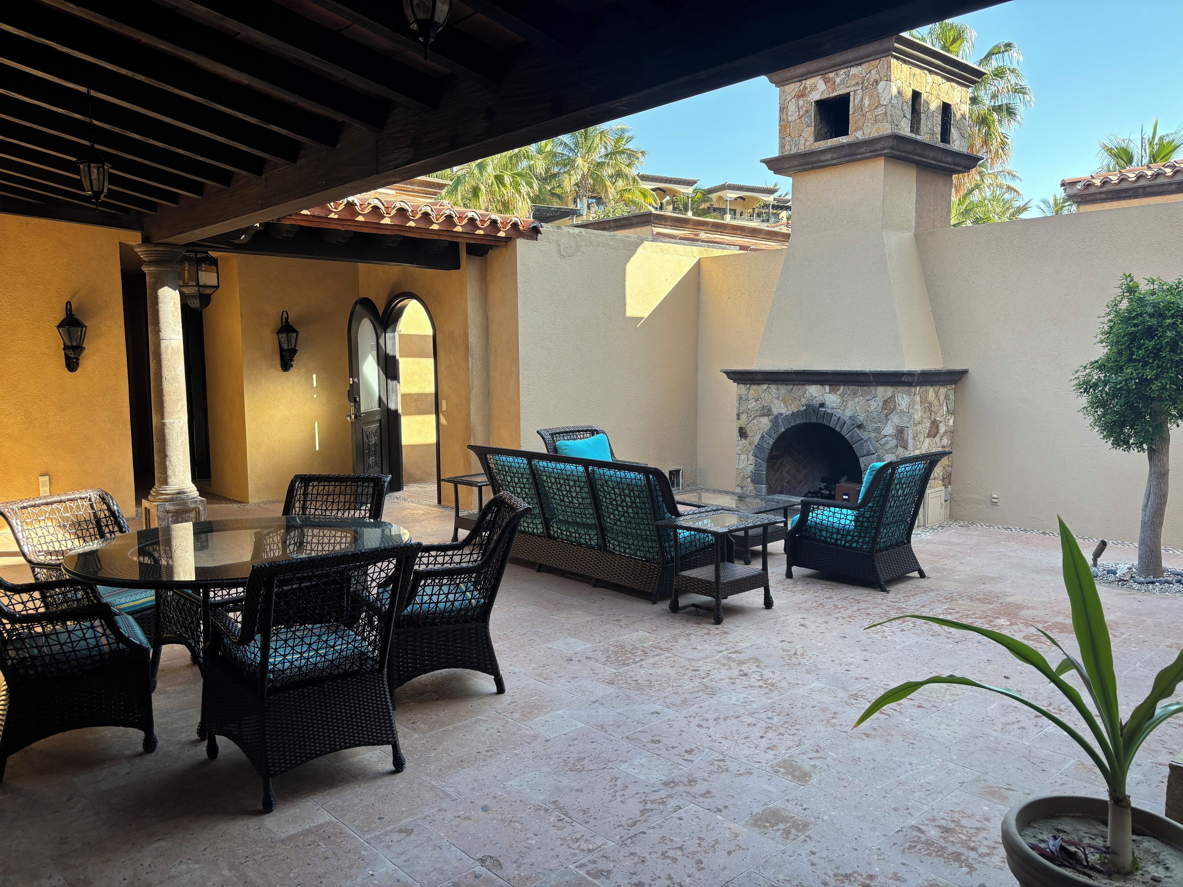 An outdoor patio with wicker furniture, a stone fireplace, and a view of a building with a tower.