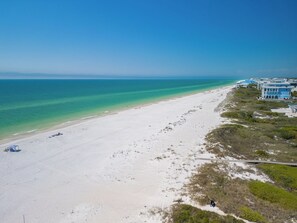 A beach with a clear view of the ocean, a sandy shore, and a row of buildings with a blue facade. - Brand New Coastal Luxury with Ocean & Bay Views, Loaded with Upscale Amenities (Cape San Blas)