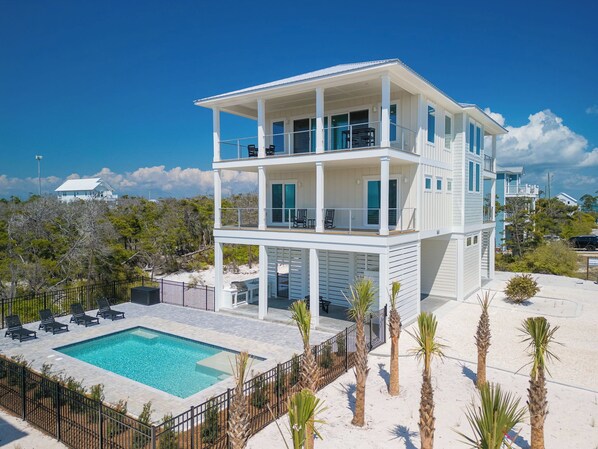 A multi-story beachfront property with a swimming pool, palm trees, and a clear view of the ocean. - Brand New Coastal Luxury with Ocean & Bay Views, Loaded with Upscale Amenities (Cape San Blas)
