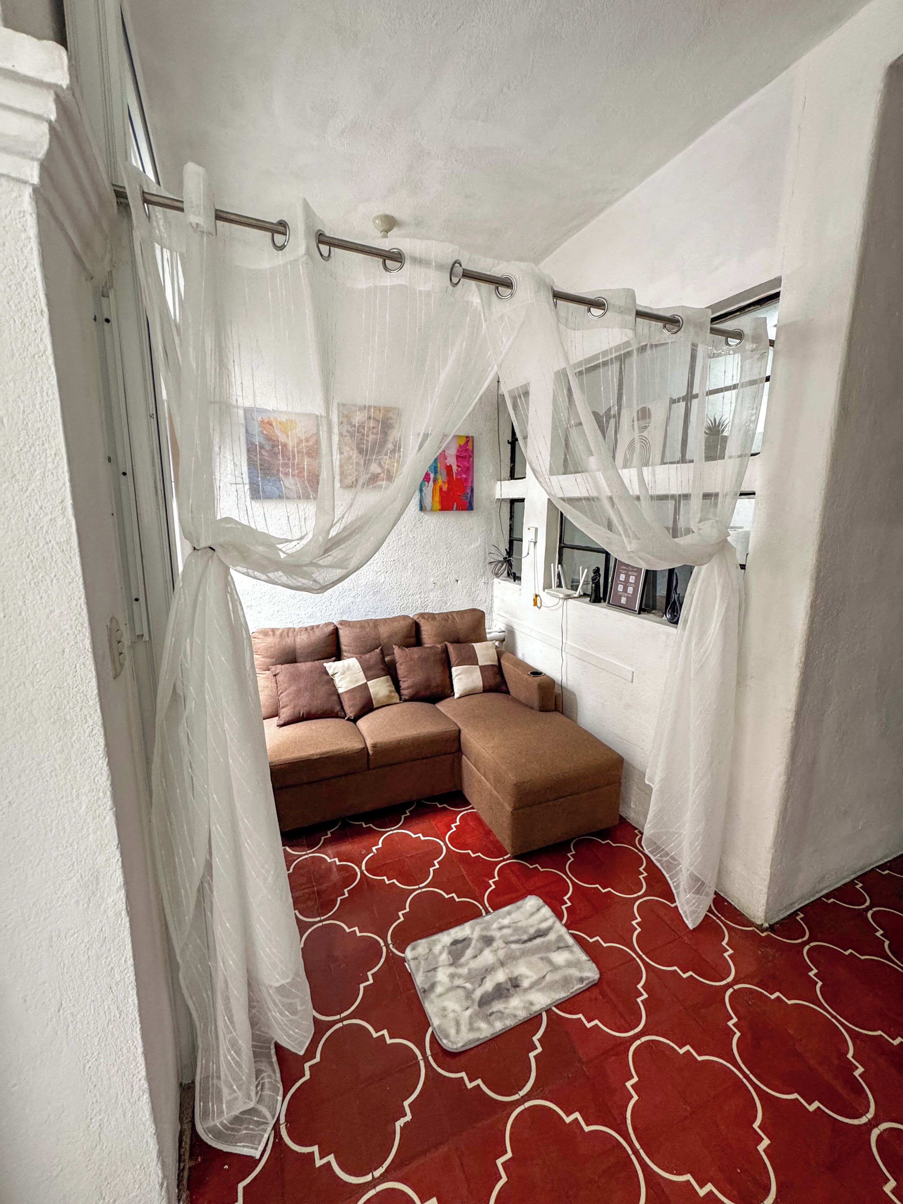 A cozy room with a sectional sofa, a patterned red carpet, and sheer curtains.