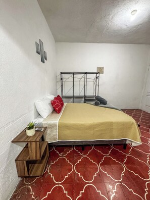 A bedroom with a bed, a bedside table, a small plant, and a patterned floor.