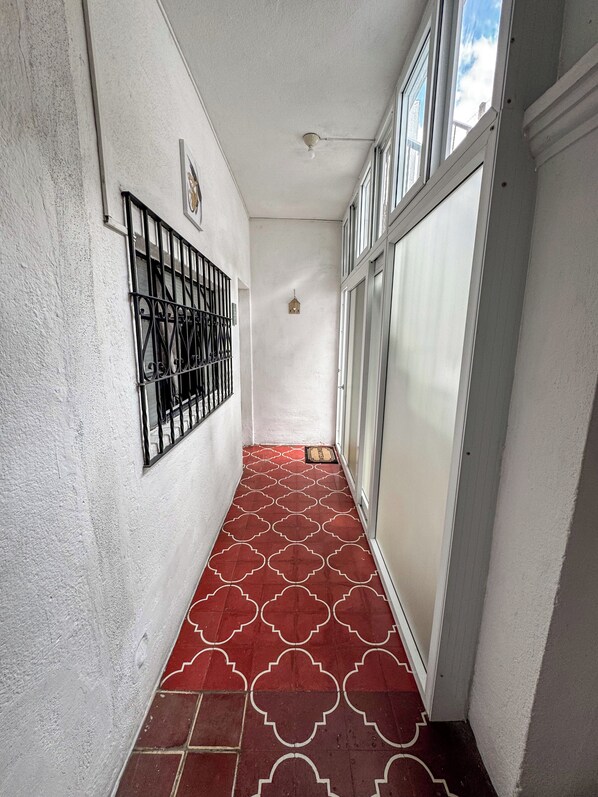 A narrow hallway with a patterned red floor, a white wall with a metal gate, and a door with frosted glass panels.