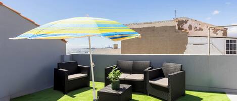 Eine Dachterrasse mit Gartenmöbeln, einem gestreiften Sonnenschirm und Blick auf die Stadt.