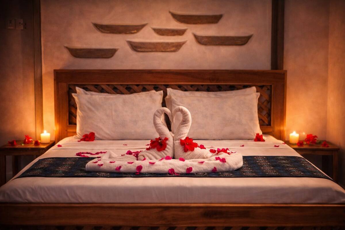 A neatly made bed with a towel artfully arranged in the shape of a bunny, surrounded by rose petals.