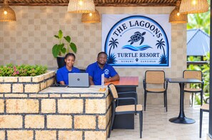 Una mesa de recepción con dos empleados, una laptop y un cartel para 'The Lagoons Turtle Resort' en Nungwi, Zanzíbar.