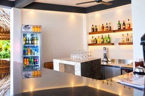 Una zona de bar con un refrigerador lleno de bebidas, una barra con vasos y estantes con botellas de licor.