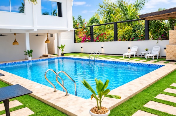 A swimming pool with a clear blue water, surrounded by a well-maintained lawn and potted plants.