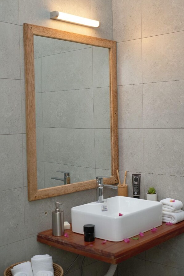 A bathroom with a wooden-framed mirror, a white sink, and a wooden vanity. - The Lagoons Turtle Resort (Nungwi)