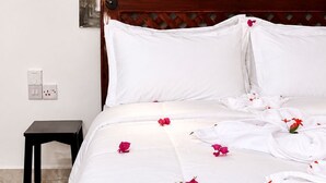 A neatly made bed with white linens and scattered rose petals, a wooden headboard, and two wall-mounted fish decorations. - The Lagoons Turtle Resort (Nungwi)