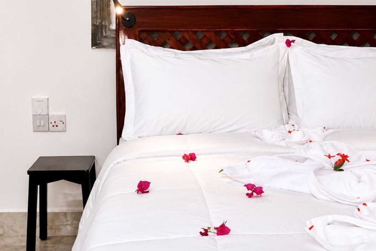 A neatly made bed with white linens and scattered rose petals, a wooden headboard, and two wall-mounted fish decorations.