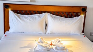 A neatly made bed with white linens and pillows, a wooden headboard, and a towel arranged on the bed. - The Lagoons Turtle Resort (Nungwi)