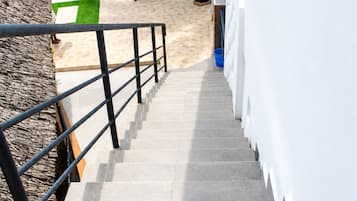 Un escalier menant à un bâtiment blanc doté d’une rampe métallique, un palmier et un ciel dégagé.