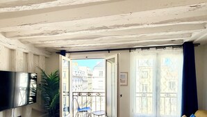 Ein Wohnzimmer mit Fischgrätparkett, einer Couch, einem Fernseher und einem Balkon mit Blick auf Gebäude.