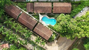 Eine Vogelperspektive zeigt ein Resort mit mehreren bungalowartigen Gebäuden, einem zentralen Swimmingpool und üppiger Vegetation.