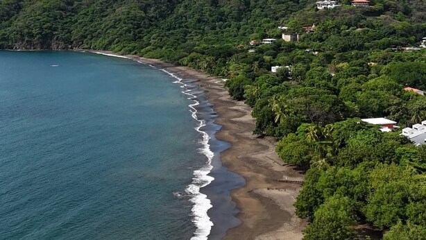 Eine Küstenlandschaft mit Strand, Grünflächen und einigen Gebäuden an einem Hügel.