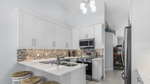 Una cocina moderna con armarios blancos, salpicadero de azulejos, una isla central con taburetes y un refrigerador.