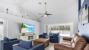 Una sala de estar con televisor, sofás y ventilador de techo.