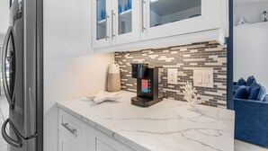 Una cocina moderna con cafetera integrada, refrigerador y un sofá azul al fondo.