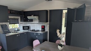 A modern kitchen with dark cabinetry, a microwave, a coffee maker, and a dining area with a wooden table and chairs. - Superb location in the Var (Fréjus)