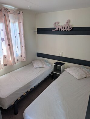 A bedroom with two single beds, a nightstand, a wall-mounted shelf, and a curtain with star patterns. - Superb location in the Var (Fréjus)