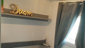 A neatly made bed with a white comforter and a plastic bag on it. Above the bed, there is a shelf with a 'Dream' sign. - Superb location in the Var (Fréjus)