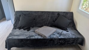 A black sofa with two black cushions and a quilted throw, positioned against a wall with a window. - Superb location in the Var (Fréjus)