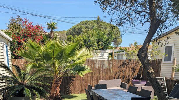 A patio area with a table and chairs, surrounded by a wooden fence and various plants. - Superb location in the Var (Fréjus)