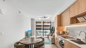 A modern kitchen with wooden cabinets, a built-in oven, and a large window overlooking a cityscape. - 501 First | Downtown 1BR | Pool & Skyline Views (Miami)