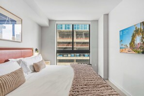 A hotel room with a bed, a large window with a view of a building, and a framed picture on the wall. - Stunning 1BR Downtown | Pool & Skyline Views (Miami)
