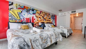 Ein Hotelzimmer mit zwei Betten, einer bunten Graffiti-Wand und einer weißen Tür.