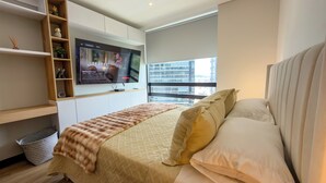 Un dormitorio moderno con cama, televisor montado en la pared y ventana con vista a la ciudad.