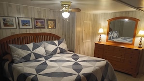 Una camera da letto con un letto, una testiera in legno, una cassettiera con specchio e quadri appesi al muro.