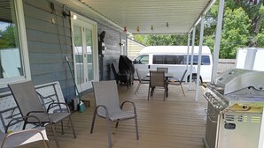 Un portico coperto con mobili da esterno, un barbecue e un furgone bianco parcheggiato nelle vicinanze.