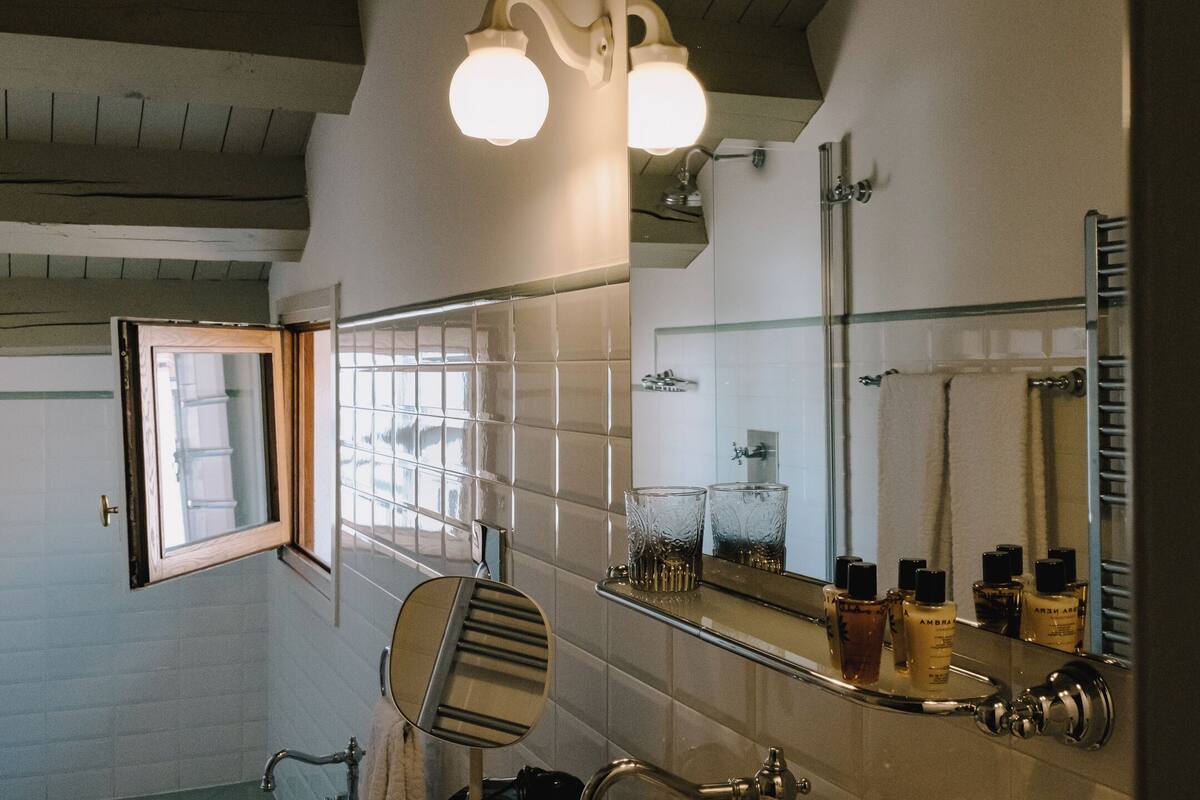 Une salle de bain avec un grand miroir, une fenêtre avec des barreaux, un porte-serviettes et des articles de toilette rangés sur une étagère.