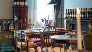 Un comedor con una mesa preparada para dos, botellas de vino en una estantería y una vela sobre la mesa.