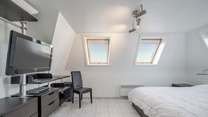 Un dormitorio moderno con cama, escritorio, silla, televisor y tragaluces.