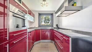 Cocina moderna con armarios rojos, horno de acero inoxidable y ventana con vista a árboles.