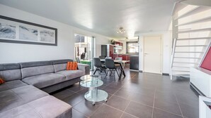 Una sala moderna con un sofá seccional gris, una mesa de centro de vidrio y una zona de comedor con una mesa y sillas.