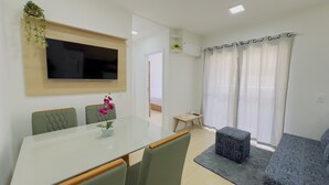 A modern living room with a flat-screen TV, a dining table with chairs, a sofa, and a small table with a plant. - Solarium Beach Club - Apartamento T2.403 (Itapoá)