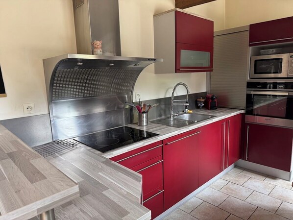 A modern kitchen with red cabinets, a stainless steel range hood, and a built-in microwave. - Near Fécamp and Etretat between sea and countryside, family house, large garden (Grainville-la-Teinturière)