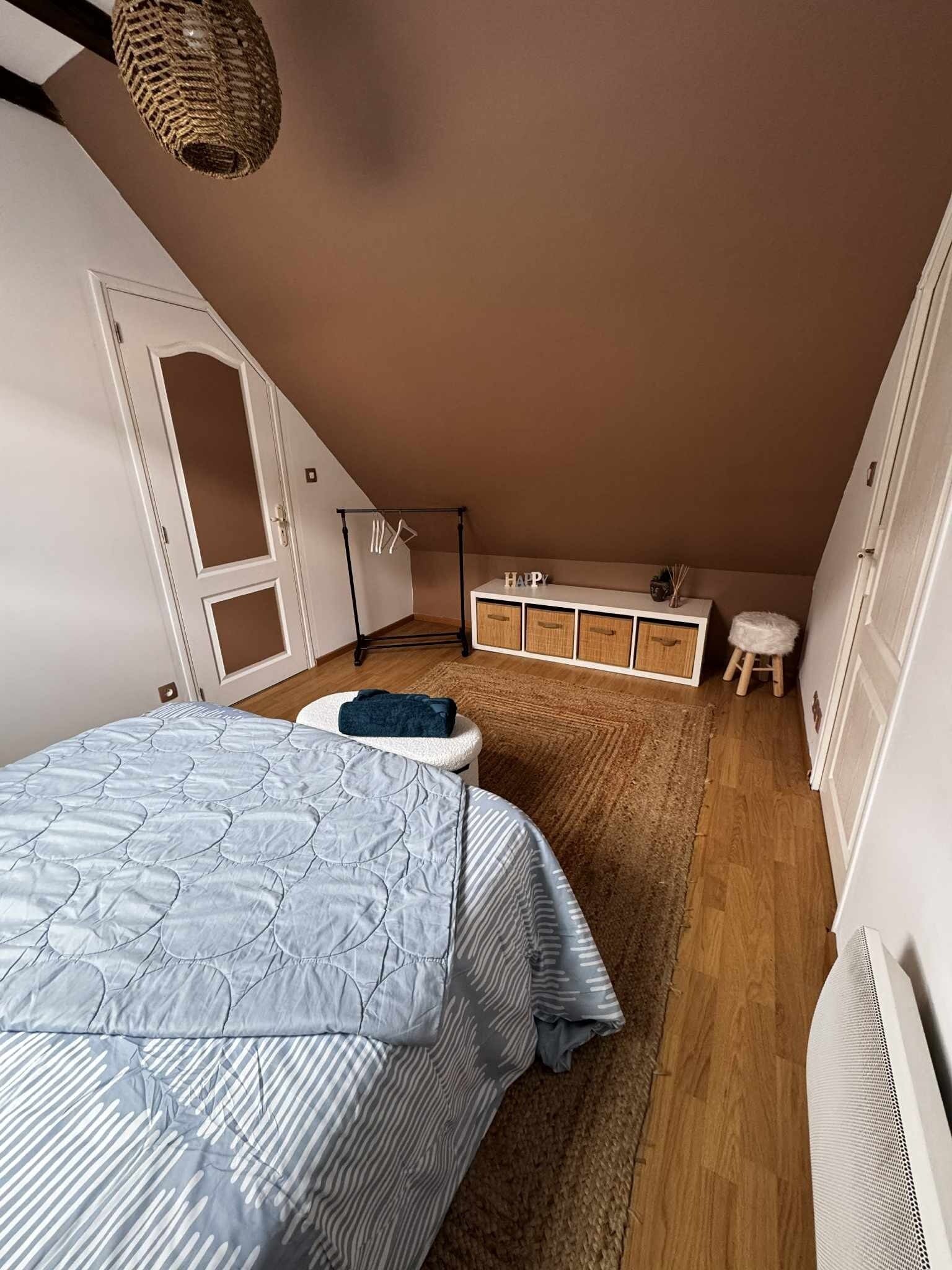 Un dormitorio con cama, cómoda, taburete y lámpara colgante.