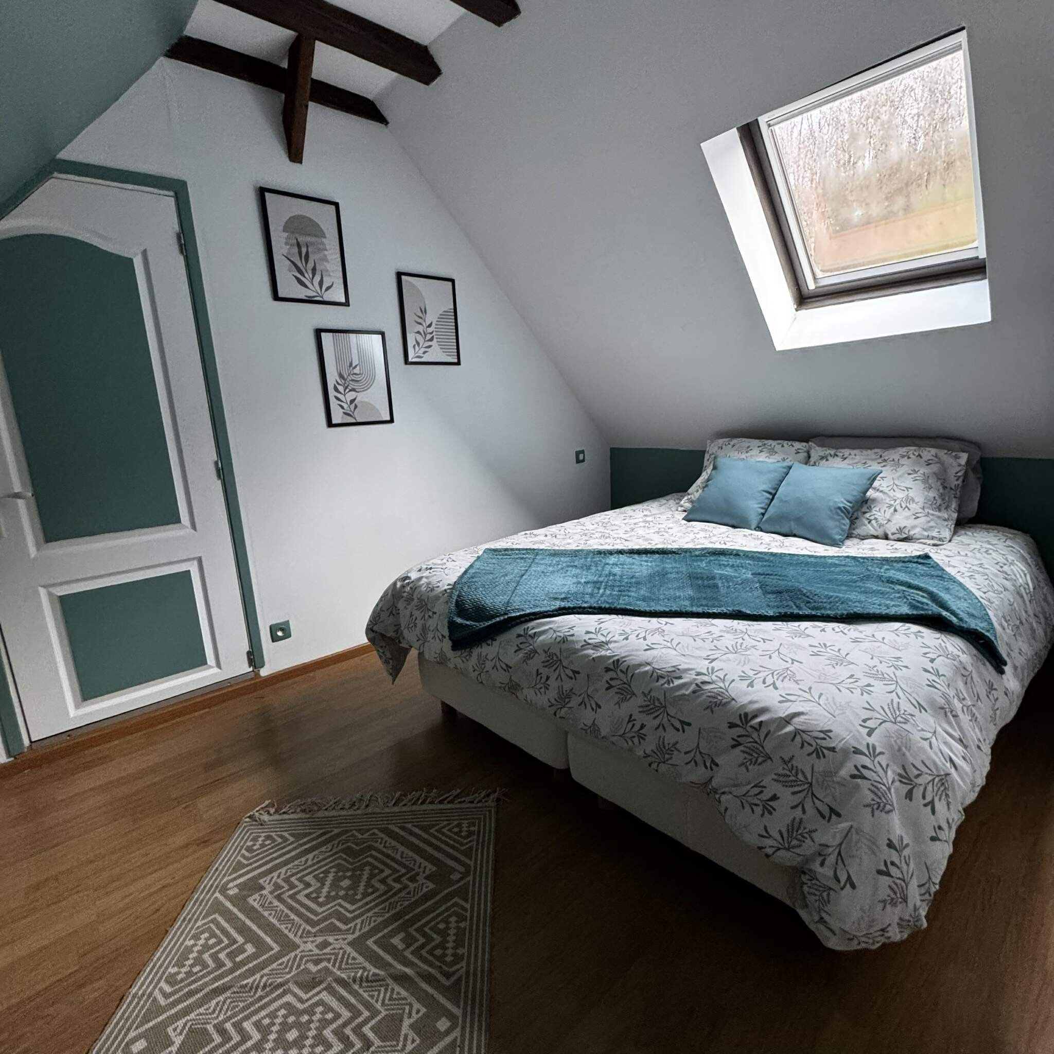 Un dormitorio con techo inclinado, una cama con ropa de cama estampada, una ventana y cuadros en la pared.