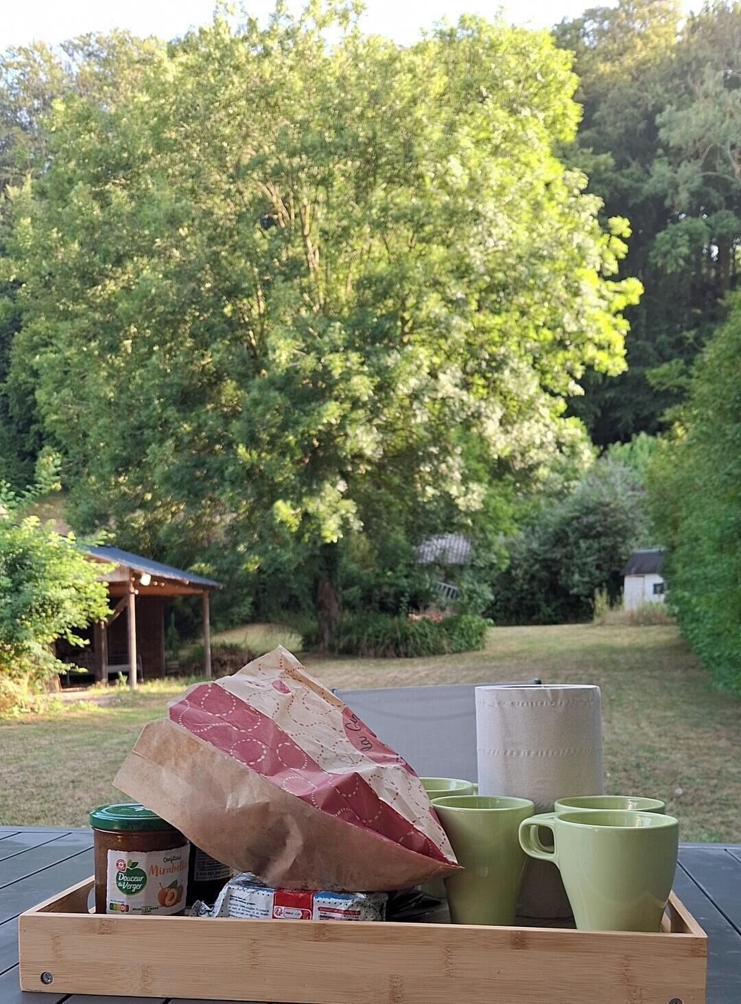 En trækasse med et syltetøjsglas, en papirspose og grønne krus på et bord.