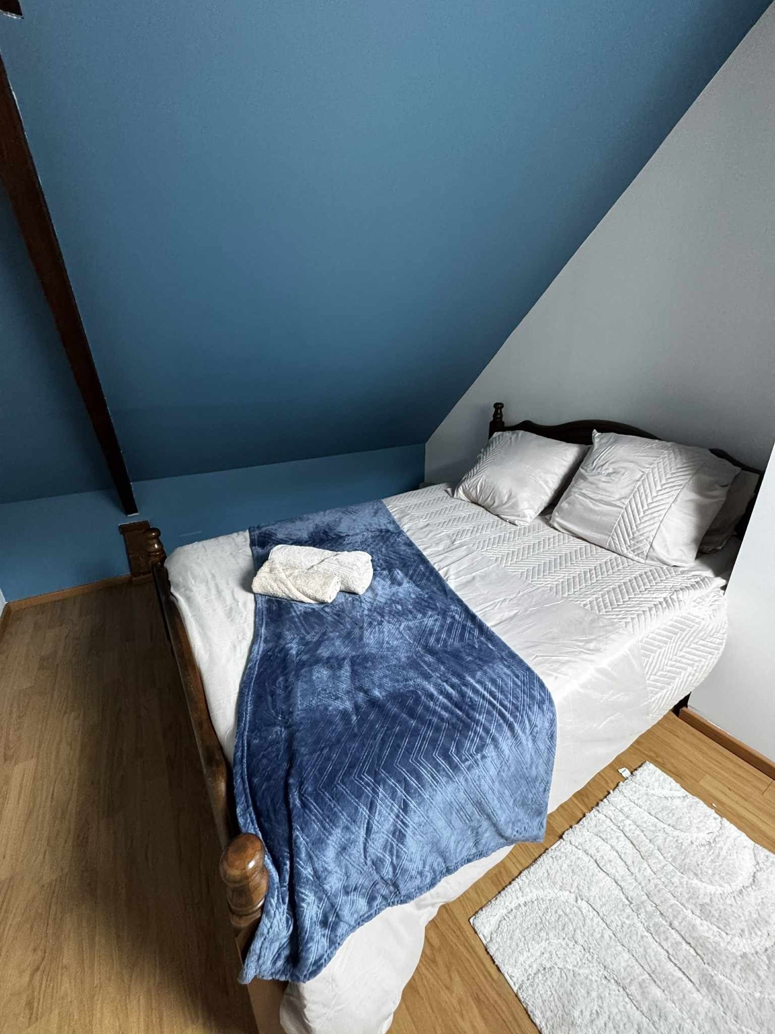 A bedroom with a bed, a blue blanket, and a white rug.